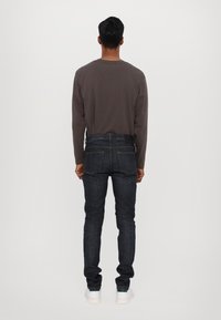 Granatowe dżinsy zaprezentowane z tyłu, charakteryzujące się slim fit, pięcioma kieszeniami oraz szarym, długim rękawem.