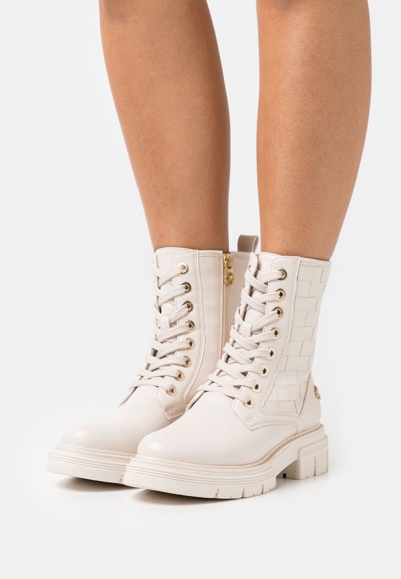 Las botas blancas hasta el tobillo cuentan con un panel tejido texturizado, punta redonda, herrajes dorados y un sistema de cordones en la parte frontal con cremallera lateral para una fácil colocación.