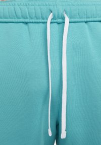 Pantalones de chándal turquesas con cierre de cordón, que cuentan con extremos de cordón blancos y una textura suave. Cintura elástica con bordes cosidos.