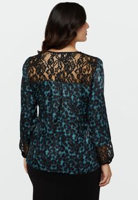 Blusa leopardata nera e turchese con dettagli in pizzo sulla schiena e sulle maniche. Tessuto morbido, forma strutturata e maniche lunghe.