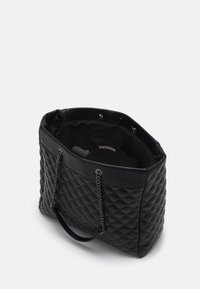 Sac cabas matelassé noir avec double poignée et accents en chaîne. Dispose d'un intérieur spacieux et d'une doublure lisse. Fermeture au sommet.