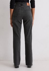 Jean noir en denim taille haute avec une jambe droite, présentant deux poches arrière et des finitions effilochées au niveau de l'ourlet. Fini avec une étiquette en cuir beige.