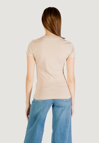 T-shirt beige a maniche corte con scollatura rotonda, design aderente e texture liscia, abbinato a jeans in denim blu a gamba larga.