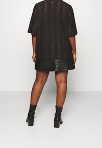 Haut noir à manches courtes avec un design en dentelle texturée et un motif ajouré. Associé à une mini-jupe en cuir et des bottines noires.