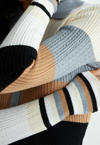 Gebreide sweater met verticale ribbels in een mix van beige, grijs, zwart en wit, met textuurpatronen op de mouwen en het lijf.