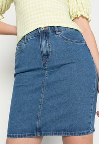 Saia de ganga em azul médio, até ao joelho, com corte recto. Apresenta um fecho de botão metálico e costura subtil ao longo das costuras.