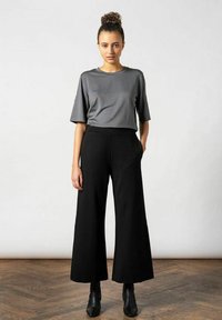 Grijze t-shirt met korte mouwen gecombineerd met hoge zwarte wijde broek. Glad tekstuur, relaxte pasvorm en zwarte enkelboots.