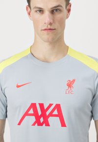 Light gray sports shirt with yellow shoulder accents, featuring a red Liverpool FC logo and red "AXA" text on the front. Short sleeves.