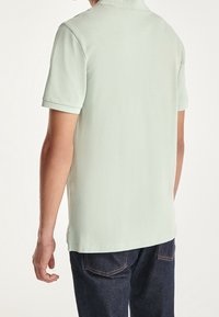 Ljusgrön pikétröja med textilstruktur, korta ärmar och ribbad krage. Bärs med mörka denimjeans. Synliga sömmar längs sidorna.