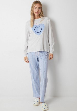 Grijs shirt met lange mouwen en een blauwe hart- en smiley-gezichtafdruk, gecombineerd met lichtblauwe gestreepte broek met kleine blauwe stippen. Witte slippers met blauwe harten.