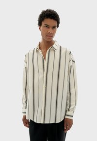 Camisa blanca de botones con rayas verticales negras, de manga larga, fabricada en un tejido suave y con un cuello clásico. Presenta un corte relajado y cierre de botones.