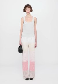 Top sin mangas ajustado gris claro con tirantes anchos, combinado con pantalones de pierna ancha con un patrón zigzag ombré de blanco a rosa. Cartera negra en la mano.
