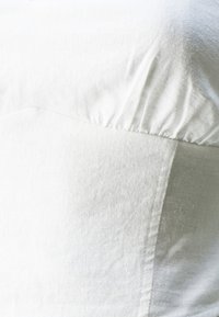 Balta tekstilė su tekstūruota paviršiumi. Yra surinkta detalė viršuje ir lygi, plokščia panelė apačioje. Raštai nematomi.