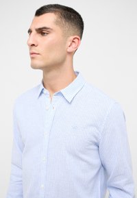 Camicia a righe blu chiaro con bottoni, dotata di colletto a punta, maniche lunghe e un piccolo logo ricamato sul petto.