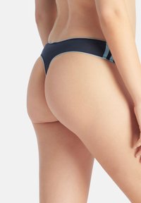 Tanga námořnicky modré barvy s hladkou texturou, minimálním krytím a kontrastními světle modrými akcenty podél okrajů.