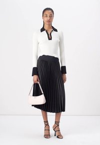 Ribbed white sweater with black collar, black pleated skirt, strappy black heels, and light pink handbag.