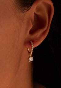 Arete de oro con un fila de pequeños rhinestones y una piedra preciosa clara más grande en el centro, llevado en la oreja.