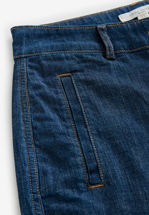 Tamsiai mėlynos džinsinės kelnės su lygia tekstūra, su oranžinėmis siūlėmis, priekinė kišenė ir juosmens etiketė.