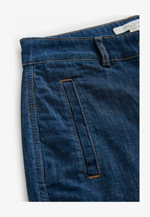 Dunkelblaue Jeans aus Denim mit einer glatten Textur, versehen mit orangen Nähten, einem Detail an der Vorderseitentasche und einem Etikett am Bund.
