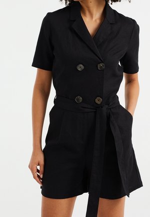 Czarny lniany kombinezon z krótkimi rękawami, podwójnymi guzikami, paskiem w talii oraz bocznymi kieszeniami. Teksturowany materiał o gładkim wykończeniu.