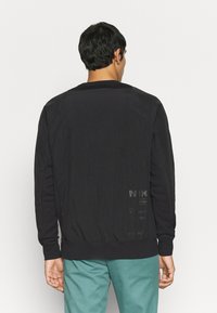 Svart sweatshirt med en jevn tekstur, med rund hals, lange ermer og trykte detaljer på baksiden. Kombinert med teal bukser.
