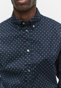 Mörkblå skjorta med knappar som har ett litet, kontrasterande geometriskt mönster. Bomullstyg med styv krage och subtil lyster.