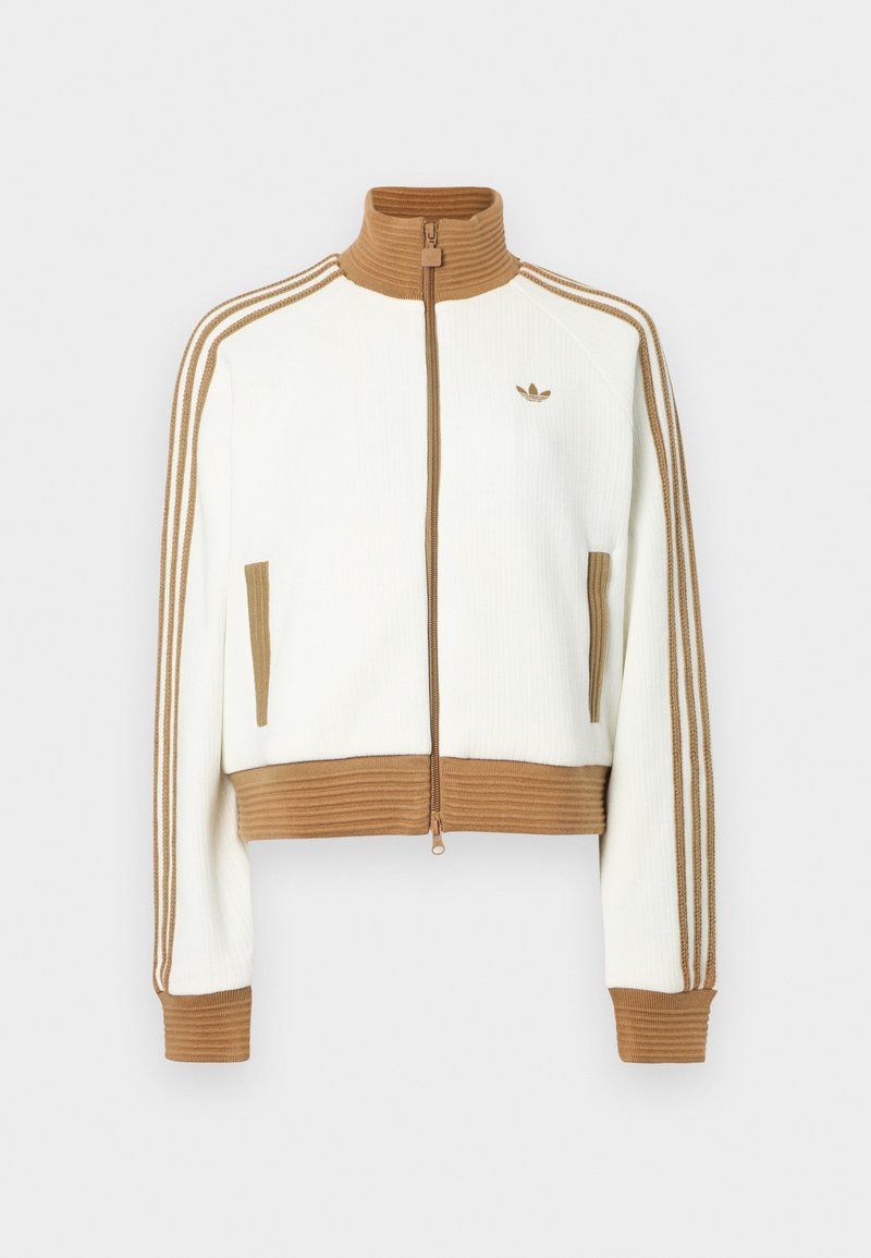 Veste blanche raccourcie avec un col et des poignets côtelés marron. Comprend deux poches latérales et trois bandes marron le long des manches. Logo brodé.