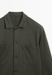 Camicia verde oliva scuro con bottoni, collo a punta, quattro bottoni sul davanti e due tasche sul petto.