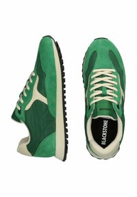 Zelené semišové tenisky s béžovými akcentmi, ktoré majú štruktúrovaný zvršok, okrúhle šnúrky a čiernu gumovú podrážku so vzorom na behu.