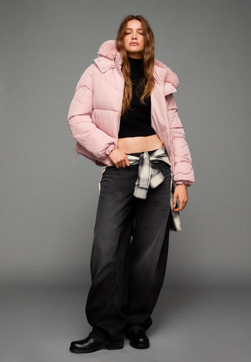 Pufasta ružičasta jakna s kapuljačom, skraćeni crni pulover, opuštene tamne traperice i crne čizme. Primjetna karirana kravata oko struka.