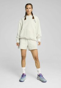 Sudadera gris claro con capucha y bolsillo frontal, combinada con pantalones cortos a juego. Zapatillas deportivas azules con acentos morados y calcetines blancos.