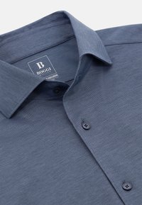 Tamsiai mėlynas mygtukais užsegamas marškinis su tekstūruotu audiniu, turintis plačią apykaklę ir du tamsius mygtukus priekyje, matomas prekės ženklas.