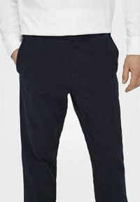 Marineblauwe broek van een gladde, matte stof, met zijzakken en een elastische tailleband voor comfort. Eenvoudig ontwerp zonder zichtbare patronen.