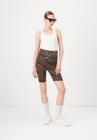 Bijela majica bez rukava u kombinaciji s crnim i smeškim tajicama s leopard uzorkom. Nosena s bijelim tenisicama i čarapama do gležnjeva. Crne sunčane naočale prisutne.