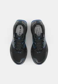 Chaussures de sport noires avec des accents bleus, tige en maille, surface texturée et semelle intermédiaire mouchetée. Les lacets sont noirs avec des détails blancs.