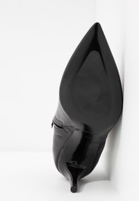Scarpa nera di pelle con tacco alto, punta affilata, texture liscia e tacco stiletto allungato. Presenta un design minimalista e senza motivi.