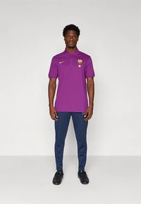 Purpurinė Nike polo marškinėliai su apykakle ir Barselonos logotipu; derinama su tamsiai mėlynomis siaurėjančiomis kelnėmis ir juodais sportiniais batais.