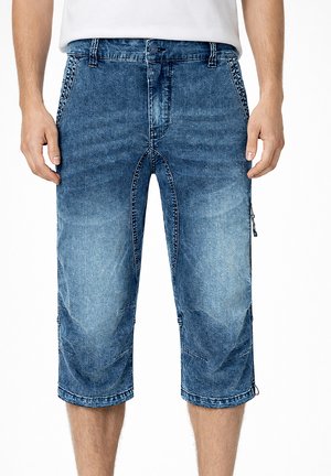 Mann trägt blaue, ausgewaschene Jeans-Knielange Shorts mit Fronttaschen und einem mit Knopf versehenen Bund, steht mit entspannt an den Seiten hängenden Händen.