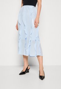 Jupe midi bleu clair avec des couches froncées et une texture brillante en sequins. Associée à des talons compensés noirs à lanières, avec un bout pointu.