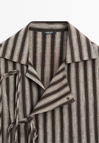 Vêtement à col avec des rayures verticales marron et beige, doté d'un rabat boutonné et de liens sur les côtés, étiqueté Massimo Dutti.