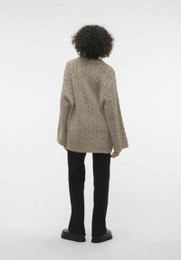 Beige cable-knit sweater with a relaxed fit, dropped shoulders, and ribbed hem, paired with black straight-leg pants and flat shoes.