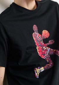 Camiseta negra de algodón con un gráfico colorido de un jugador de baloncesto en el aire, con formas y patrones vibrantes y pixelados.