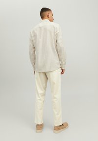 Light striped button-up shirt with long sleeves, cream trousers, and beige sneakers. Minimal design in neutral tones and relaxed fit.
