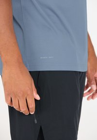 Nopea kuiva sininen urheilu paita yhdistettynä mustiin shortseihin. Paidassa on sileä rakenne ja pieni logo helman lähellä. Shortseissa on sivutaskut.