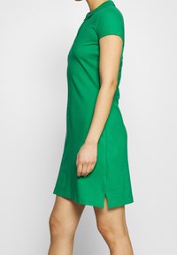 Vihreä puuvillapolo-mekko, jossa on klassinen kaulus, lyhyet hihat, sivureikä ja vartalonmyötäinen muoto.
