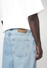 Lichtblauwe denimjeans met een relaxte pasvorm, voorzien van een leren label met de inscriptie "EIGHTYFIVE" en twee achterzakken.