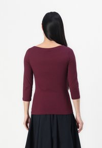 Burgundy, figurnära topp med trekvartsärmar i mjukt tyg, med en vid, rund halsringning och en ren fåll, kombinerad med en svart kjol.