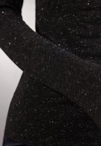 Sort langærmet top lavet af struktureret stof med subtile glimt, der har tætsiddende ærmer og en glat finish.