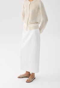 Lett og gjennomsiktig beige cardigan med rund hals og knapper, tilpasset en glatt hvit midi-skjørt og taupe sandaler med kryssremmer.