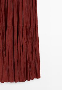 Textured, dark rust-colored fabric drapes with vertical pleats, creating a flowing design. The background is plain white.